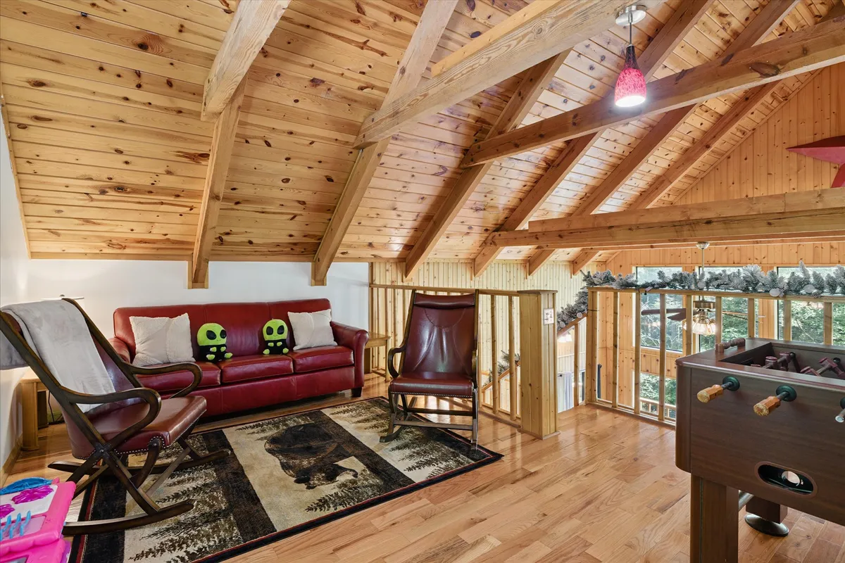 A spacious, cozy interior game room features a red sofa, foosball table, rocking chair, and exposed wooden beams. The space is designed for family game nights, laughter, and comfortable relaxation after exploring local attractions.