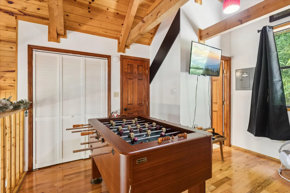 A cozy interior with a foosball table set near large windows, wooden beams, a television, and plenty of space for socializing. The room exudes a fun and relaxed vibe, ideal for game nights and casual lounging.
