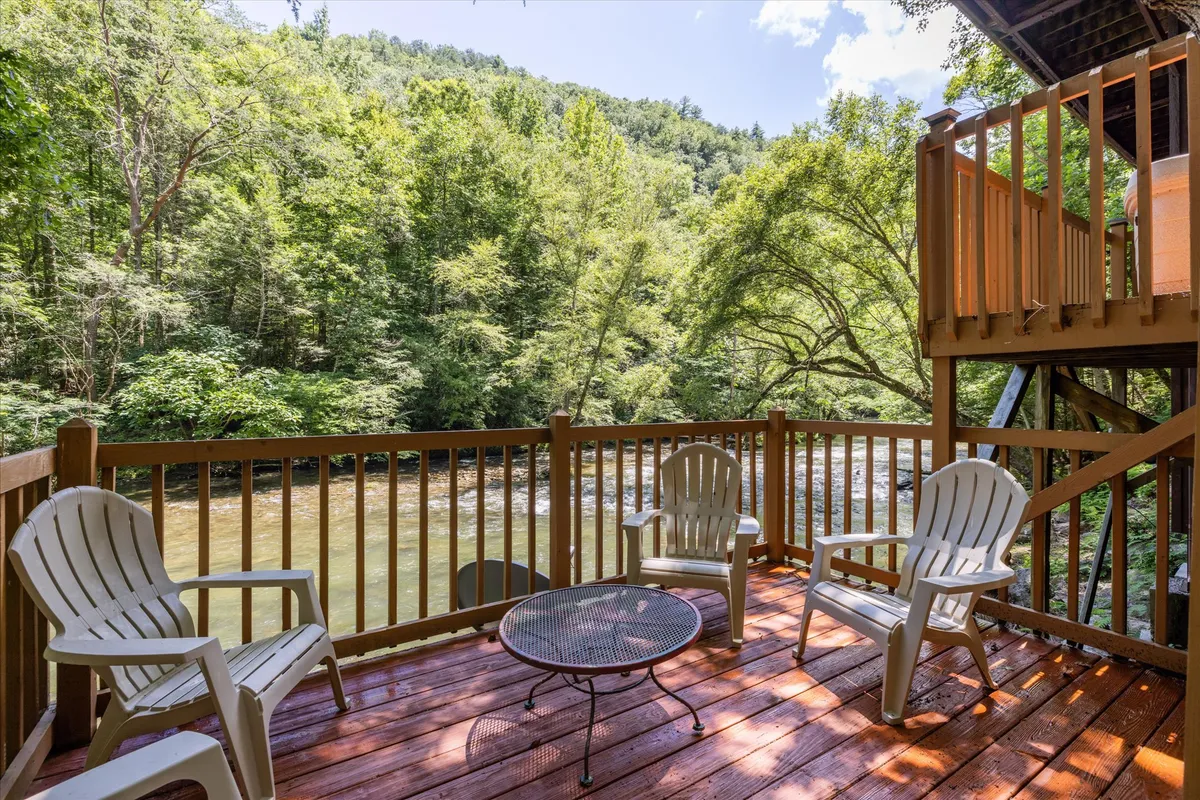 A peaceful wooden deck with classic Adirondack chairs facing a stunning river view, bordered by lush greenery. The deck invites moments of relaxation, whether for morning coffee, reading, or simply enjoying the river's gentle presence, underscoring the seamless transition between indoor comfort and outdoor beauty.
