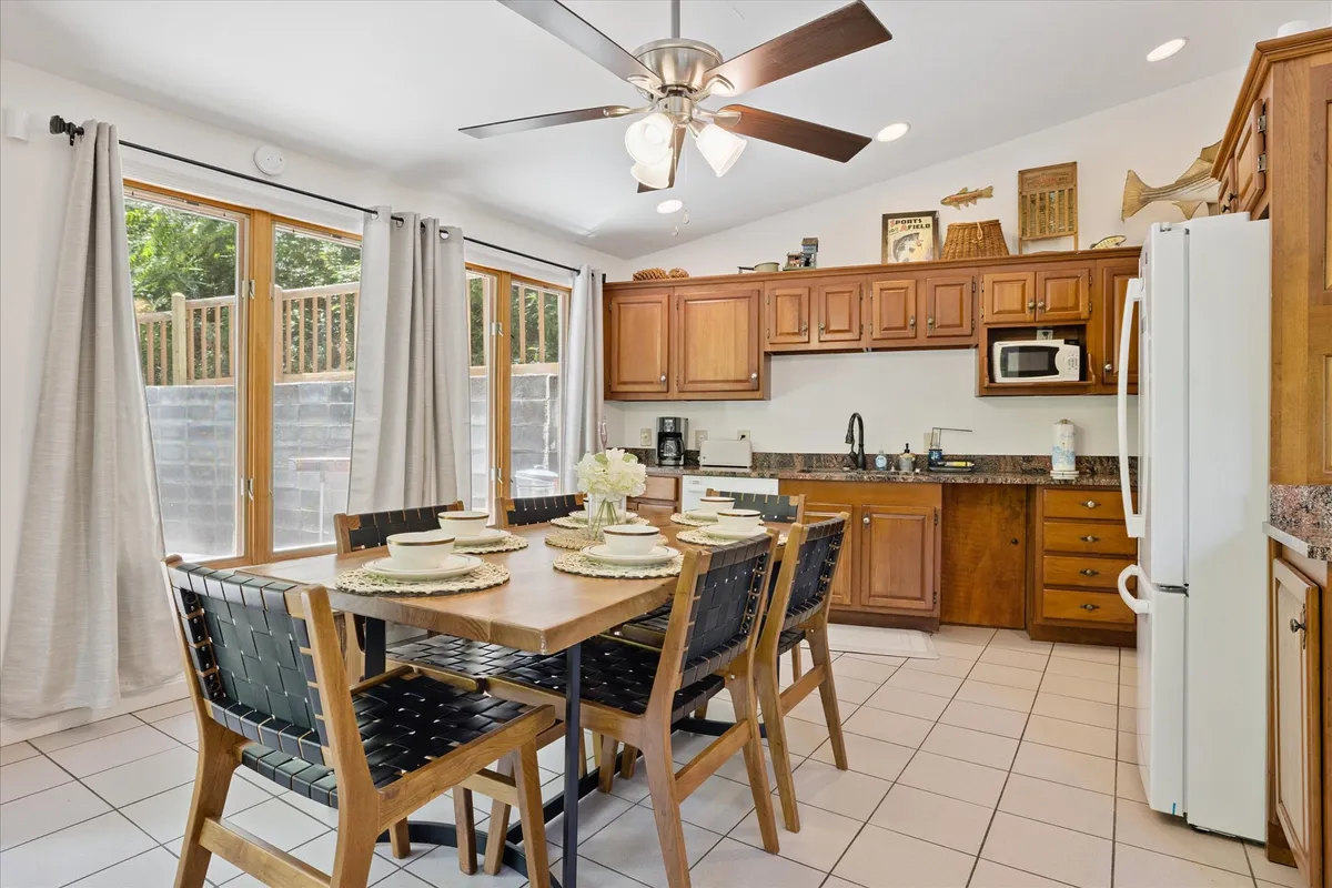 A wide-angle shot of a spacious dining table adjacent to kitchen cabinetry and large windows that let in plenty of natural light. The scene suggests a welcoming space for gatherings, with the table able to accommodate a group and the kitchen easily accessible. The ambiance is warm, suitable for both quick breakfasts and lingering dinners while enjoying views outside.