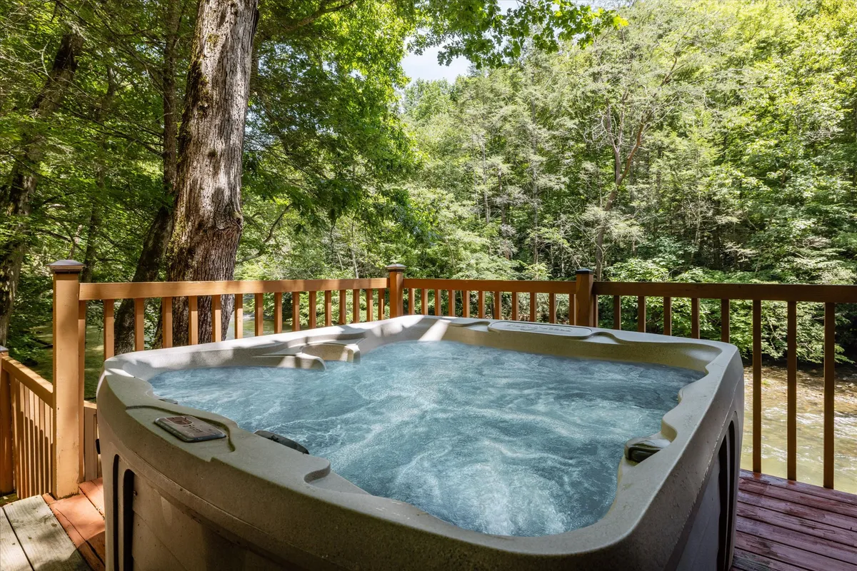 A steaming hot tub sits on a wooden deck, surrounded by tall trees and the soothing sounds of nature. The deck overlooks the forest, offering a private spot for relaxation, stargazing at night, and bonding after a day of adventure.