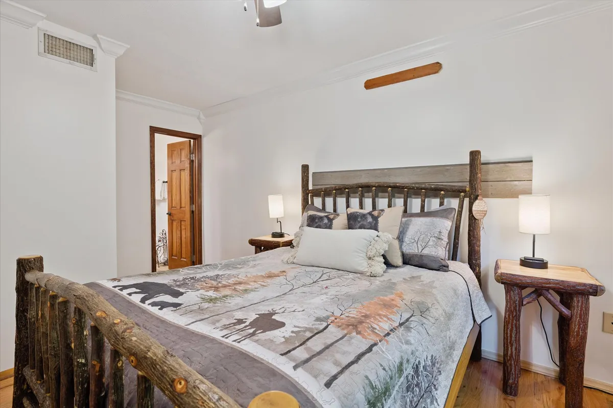 A tranquil bedroom featuring a rustic log bed frame with decorative bedding, flanked by nightstands and softly glowing lamps. The room is bathed in gentle natural light, creating a cozy and restful atmosphere ideal for relaxation or reading.